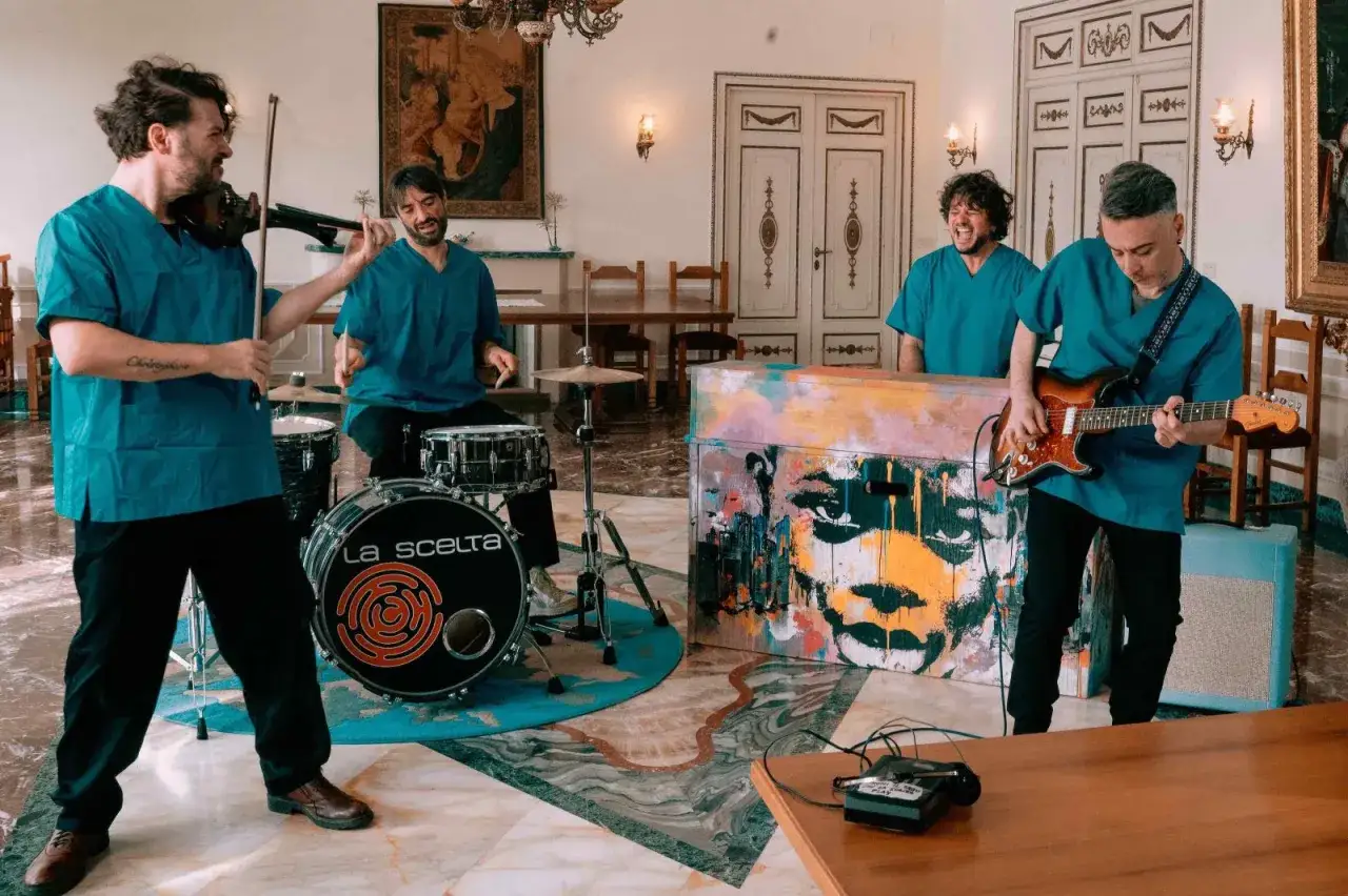 Quattro musicisti in camici blu suonano in una stanza elegante, con un dipinto di un volto su un pianoforte. La loro musica sembra sfidare questo eterno decadimento.
