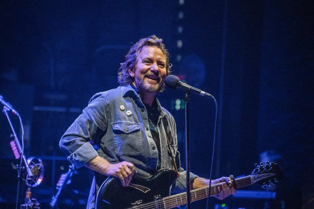 Eddie Vedder sorride mentre suona la chitarra sul palco, un'icona della band.
