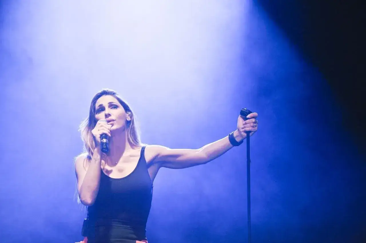 Anna Tatangelo canta sul palco, illuminata da luci blu. Le sue canzoni emozionano il pubblico.
