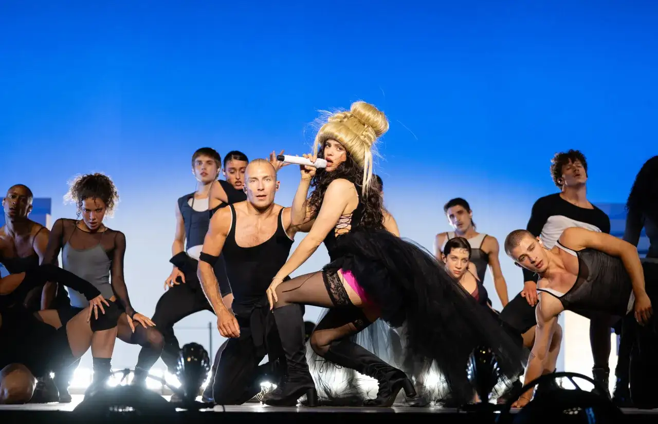 Rosal&iacute;a, la cantante spagnola, domina il palco con un microfono, circondata da ballerini in un'esibizione energica.