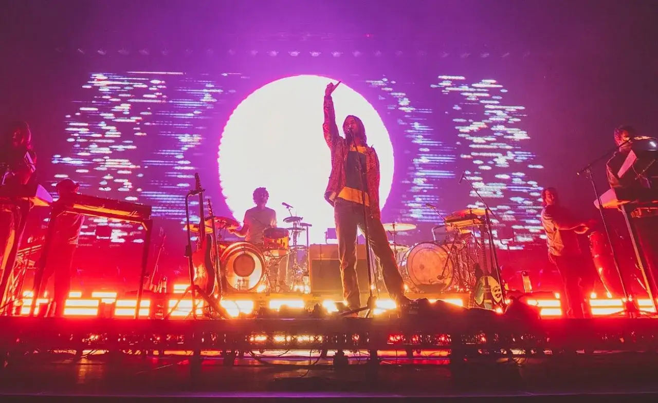 I membri dei Tame Impala sul palco, con un grande sole sullo sfondo e luci psichedeliche.