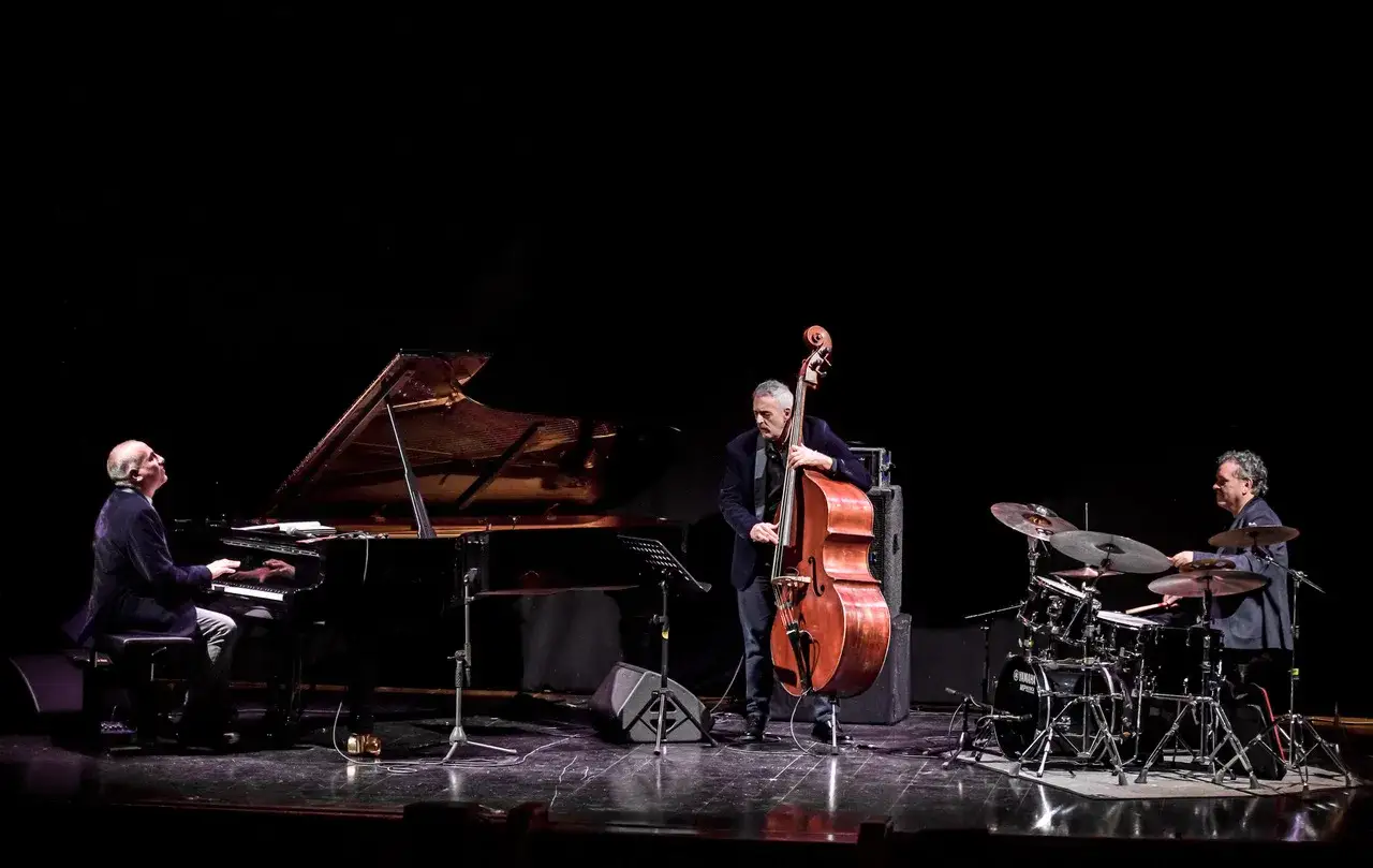 Trio jazz sul palco: pianista, contrabbassista e batterista. John De Leo, con il suo contrabbasso, è al centro della scena.