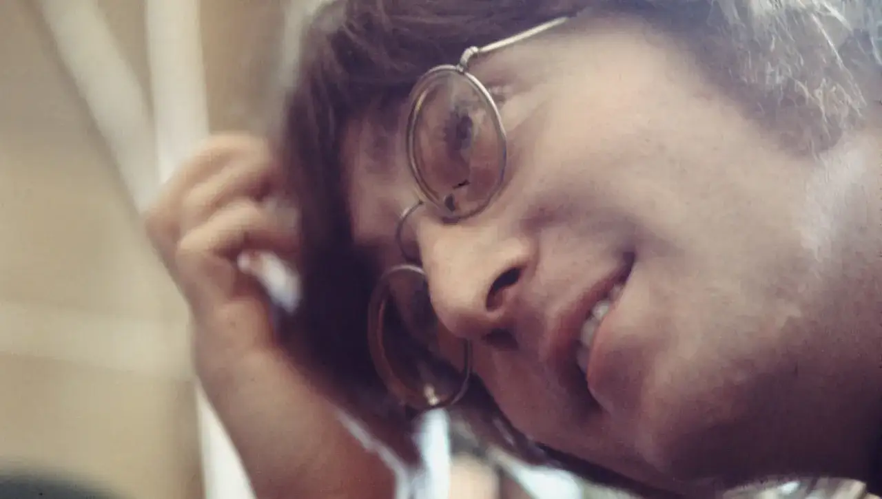 Primo piano di John Lennon con occhiali rotondi, mentre si tocca i capelli. Un'immagine che evoca le sue iconiche canzoni.