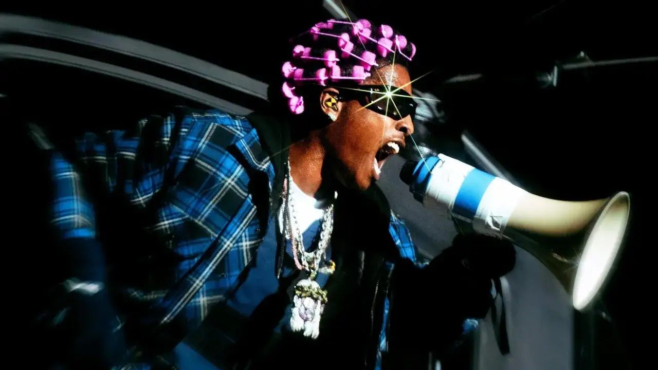Giovane rapper italiani con capelli cotonati rosa, occhiali da sole e megafono, grida con energia.