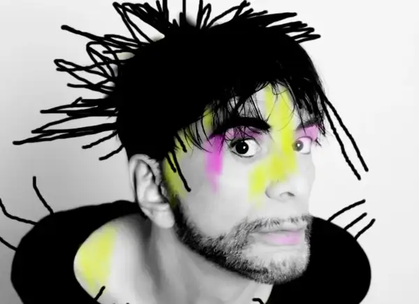 Ritratto di Ivan Cattaneo con capelli neri a punta, trucco colorato e barba. Le sue canzoni sono uniche.
