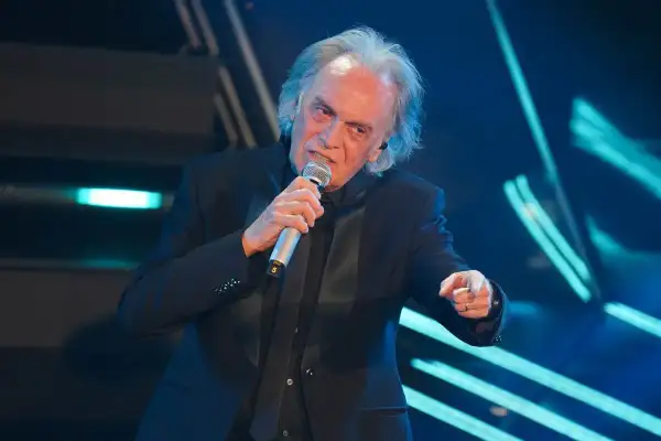 Riccardo Fogli canta sul palco, con il microfono in mano, evocando le sue indimenticabili canzoni.