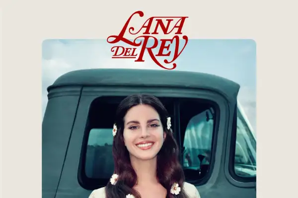Lana Del Rey sorride, con fiori tra i capelli, accanto a un vecchio camion. Un'immagine che evoca il suo "lust for life".