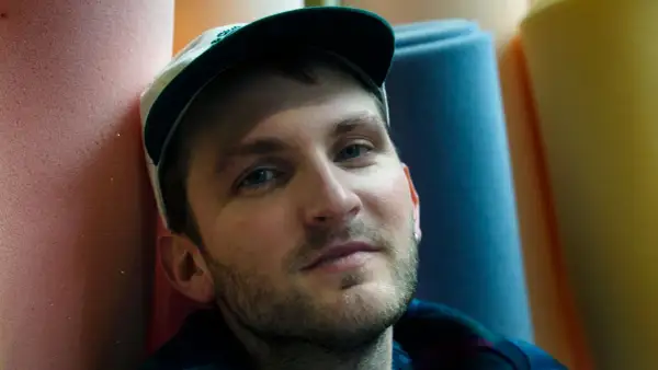 Ritratto di un uomo con cappellino, circondato da rotoli di gommapiuma colorata. Le sue canzoni di Giorgio Poi evocano immagini vivide.