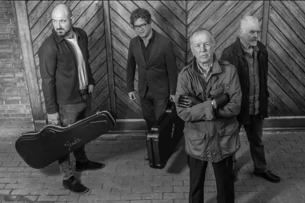 I membri di the Animals, quattro uomini con valigie per strumenti musicali, posano davanti a un portone di legno.