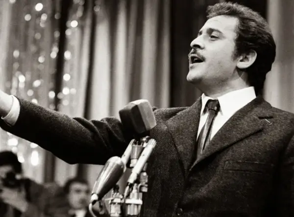 Domenico Modugno, originario di Polignano a Mare, canta con passione al microfono, con il braccio teso.