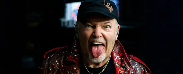 Vasco Rossi, con la lingua fuori e un'espressione grintosa, indossa una giacca borchiata. Chissà quante canzoni ha fatto Vasco Rossi per arrivare a tanta energia!