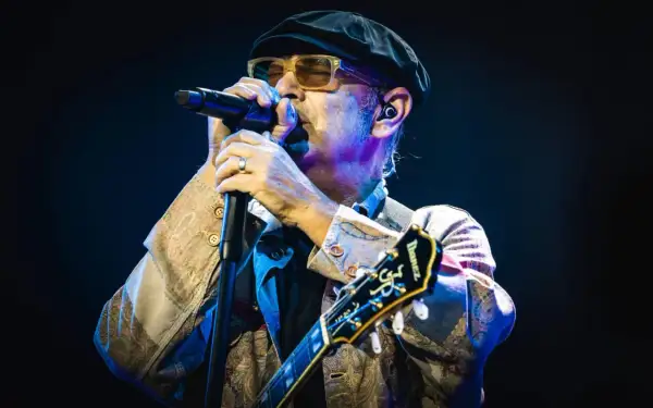 Luca Carboni canta "Le storie d'amore" con passione, chitarra in mano, sotto le luci del palco.