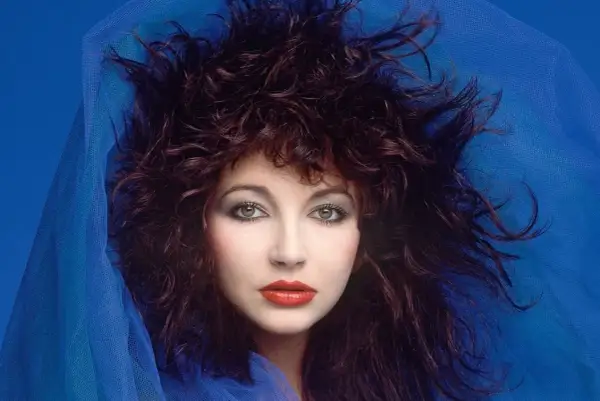 Ritratto di Kate Bush con capelli scuri e fluenti, occhi verdi penetranti e labbra rosse, avvolta in un velo blu. Un'icona delle canzoni di Kate Bush.