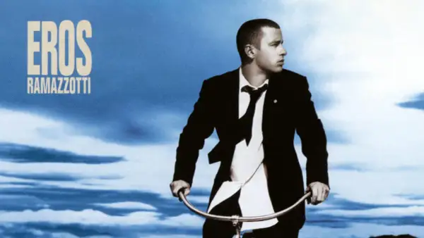 Copertina album di Eros Ramazzotti con lui in giacca e cravatta su una bicicletta sotto un cielo blu.