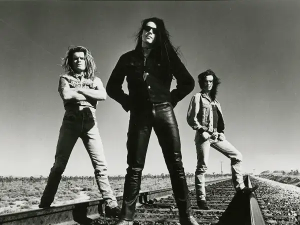 I membri dei The Cult posano sulle rotaie in un paesaggio desertico, con un cielo limpido sullo sfondo.