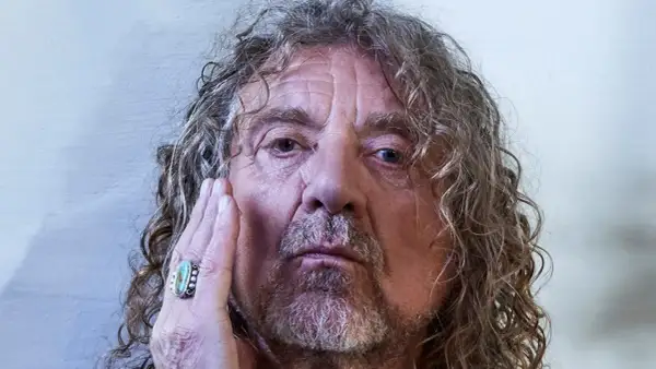Primo piano di Robert Plant, con la mano sul viso, un anello turchese. La sua espressione è intensa, quasi una saving grace per chi lo osserva.