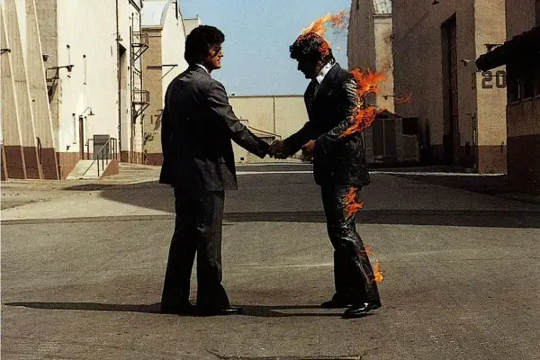 Due uomini si stringono la mano, uno in fiamme. Un'immagine iconica che evoca il "wish you were here significato" di assenza e desiderio.